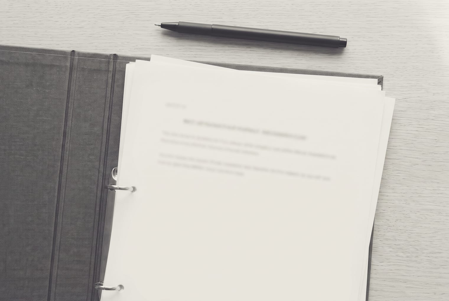 Tampak atas berkas kerja di atas meja: setumpuk kertas di dalam ring binder dengan satu pena di sisinya. Isi teksnya tidak terbaca.
